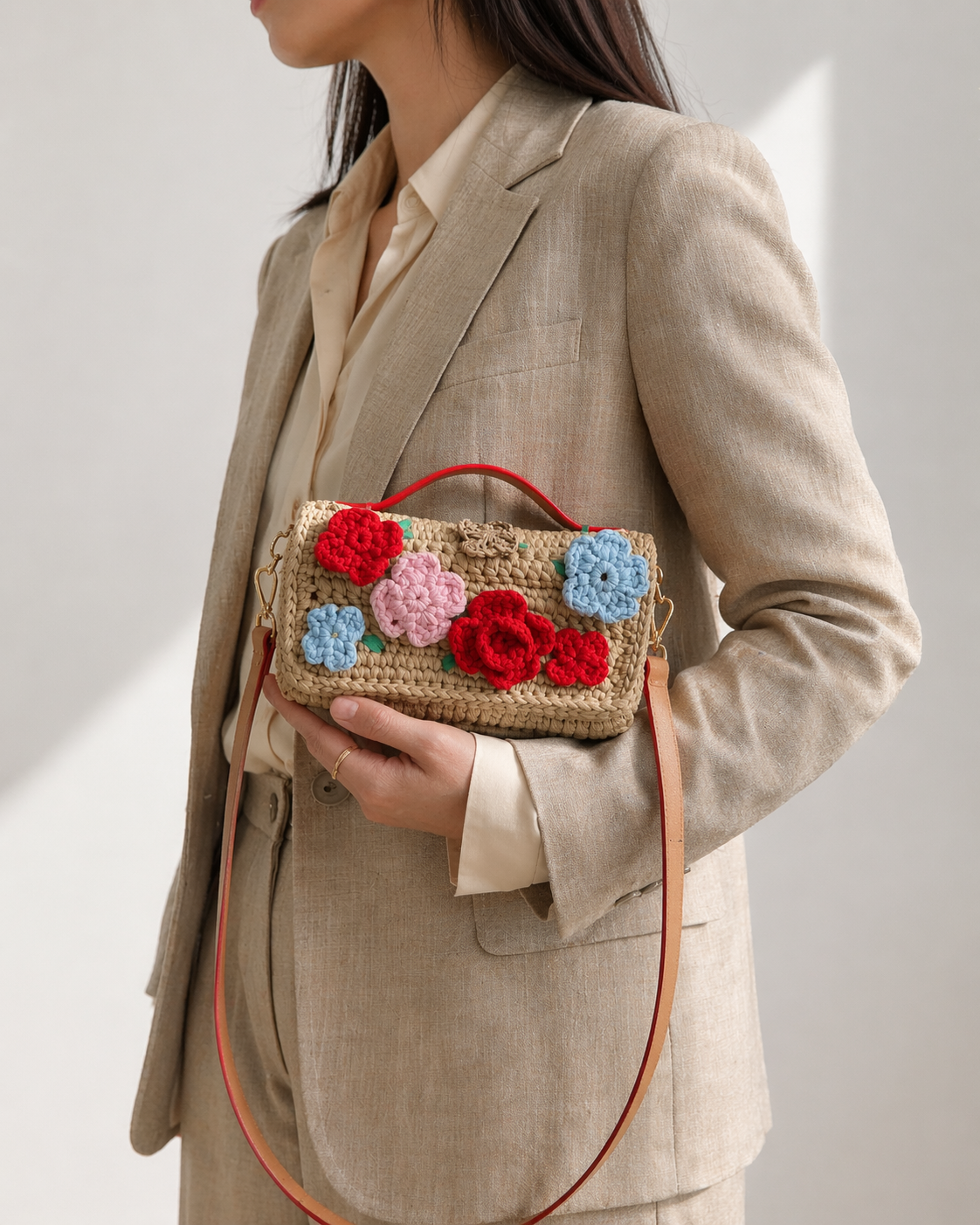 Person wearing a beige suit holding a crochet handbag with floral decorations.
