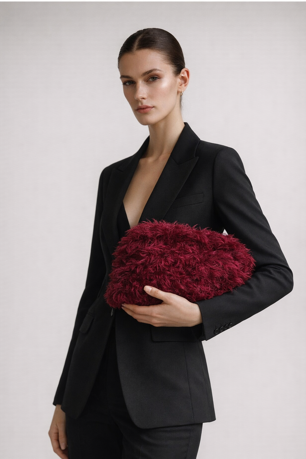 Woman in a black suit holding a red clutch against a plain background